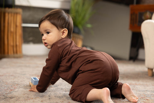 Baby in a brown outfit crawling on a carpeted floor.