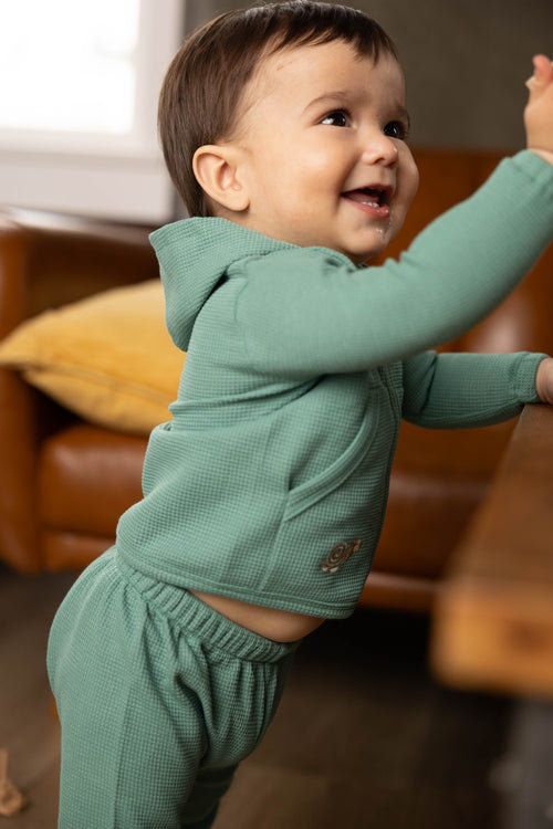 Child in a green outfit standing in a living room