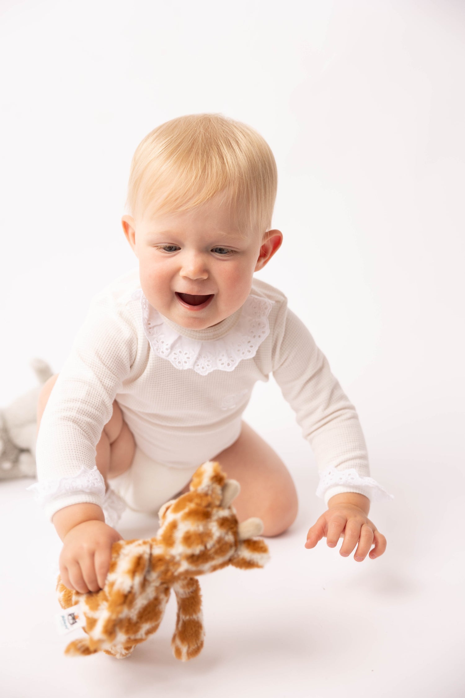 Baby in a white outfit with a giraffe toy on a white background