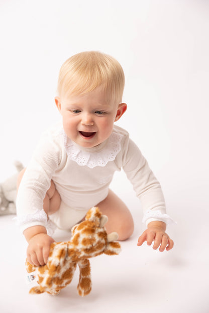 Baby in a white outfit with a giraffe toy on a white background
