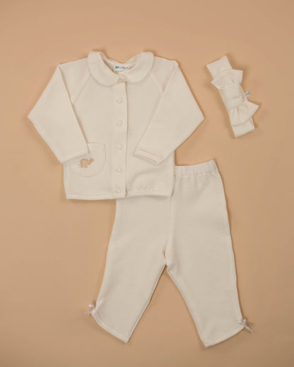 A baby girl's white waffle 2 piece set with a sweatshirt featuring a collar and a button placket, and matching pants with a bow detail at the ankles, presented on a beige background.
