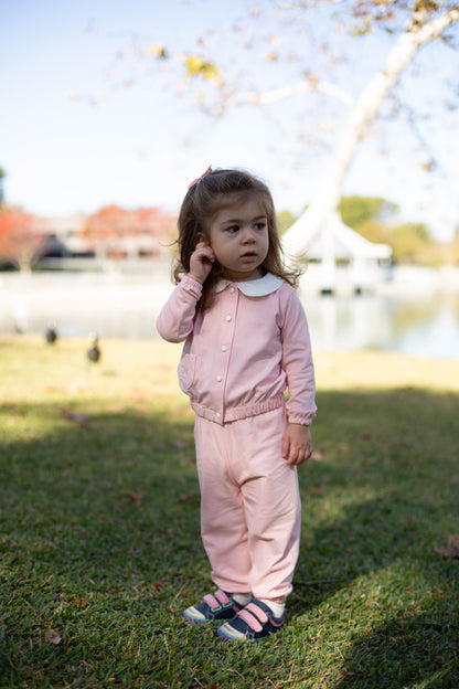 Young girl in a pink outfit standing outdoors with a blurred background